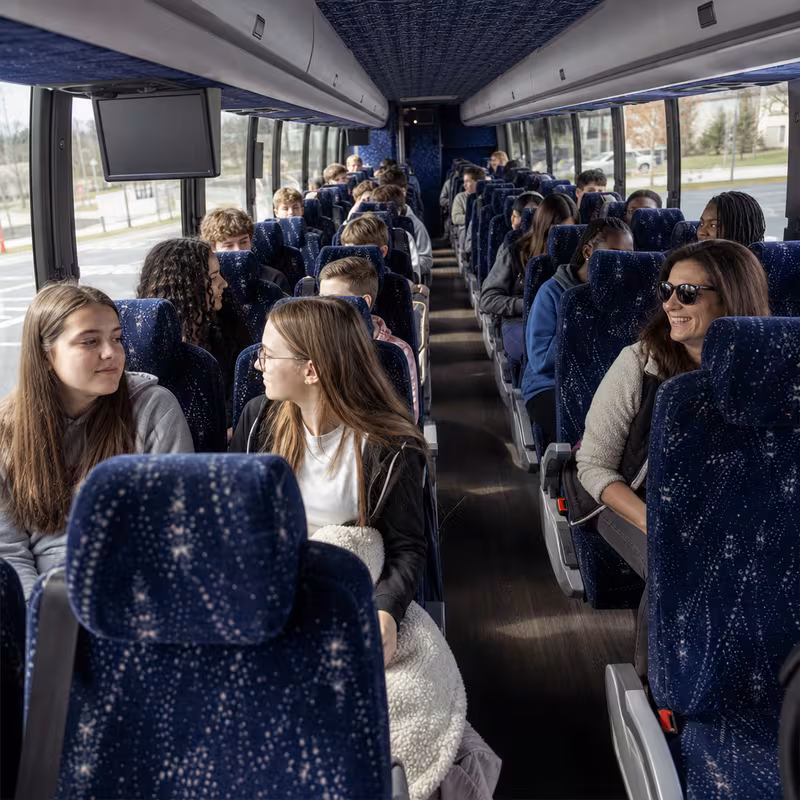 Group boarding a white charter bus for School Transportation transportation in Sterling Heights